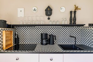 Eine Küche mit einem schwarz-weißen Spritzschutz, einer Kaffeemaschine, einem Spülbecken und einer an der Wand montierten Uhr.