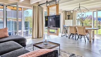 A spacious living room with a large TV, comfortable seating, and a dining area with natural light.