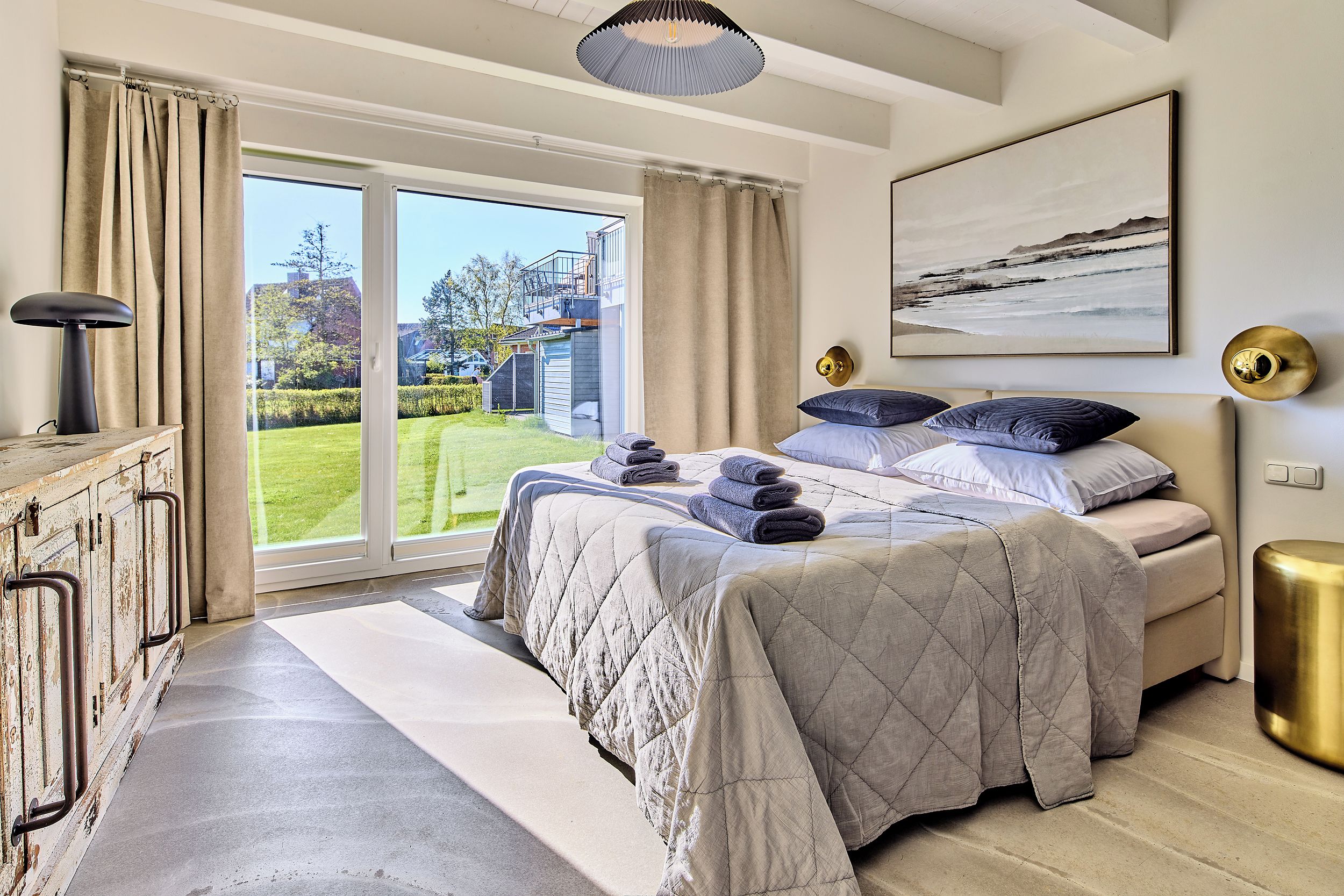 Une chambre à coucher avec un lit, une table de chevet, une lampe, un tableau et une vue sur l’extérieur.