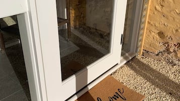 Une porte blanche avec un panneau de verre, un paillasson sur lequel est écrit « Bienvenue », et un chemin de gravier menant à la porte.