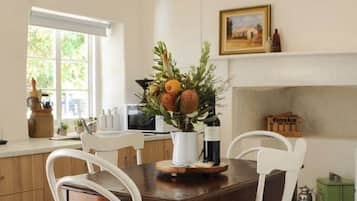 Un coin repas avec une table en bois et des chaises blanches, un vase rempli de fleurs et une cheminée en arrière-plan.