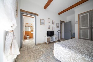 A bedroom with a bed, a television, a wardrobe, and a bathroom visible through an open door. - Mas de la Bimarde (Monteux)