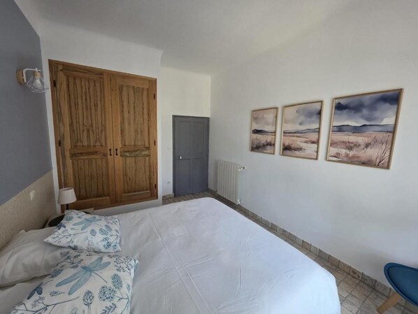 A bedroom with a large bed, a wardrobe, a radiator, and three landscape paintings on the wall.
