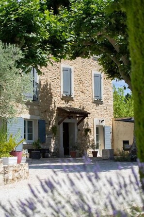 A stone building with a covered entrance, potted plants, and a gravel driveway. - Mas de la Bimarde (Monteux)