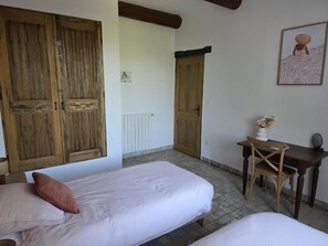 A room with two beds, wooden wardrobes, a desk with a chair, and a wall-mounted picture.
