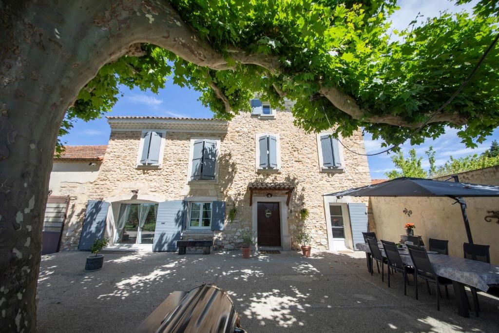Un edificio de piedra con un patio techado, mobiliario exterior y un árbol que da sombra.