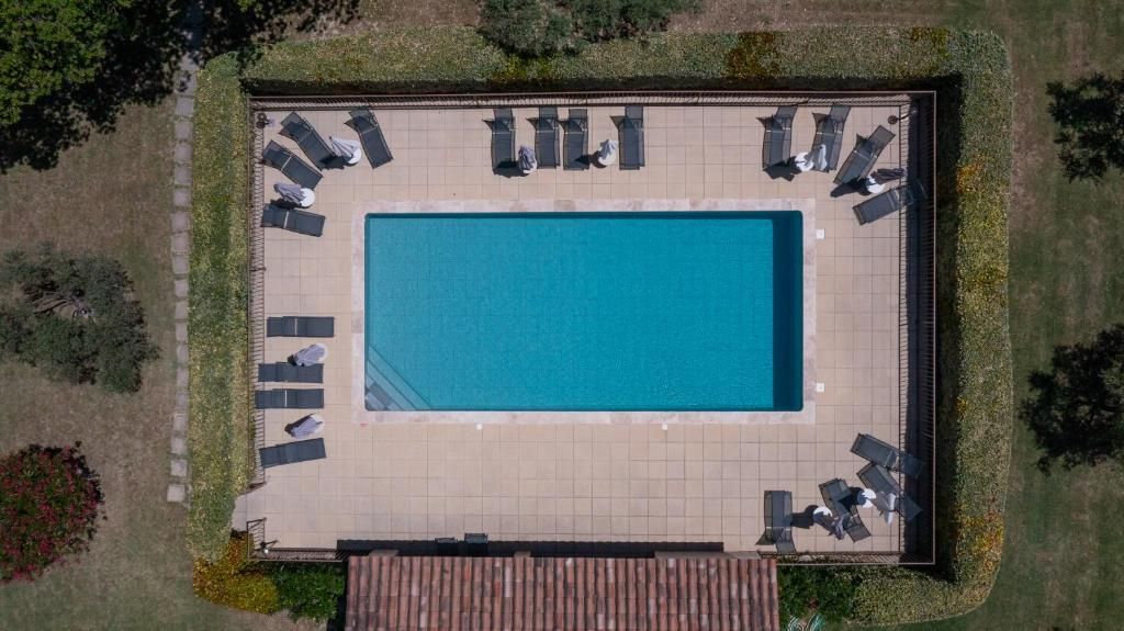 An aerial view of a rectangular swimming pool with a tiled deck, surrounded by lounge chairs and umbrellas.