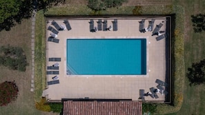 An aerial view of a rectangular swimming pool with a tiled deck, surrounded by lounge chairs and umbrellas.