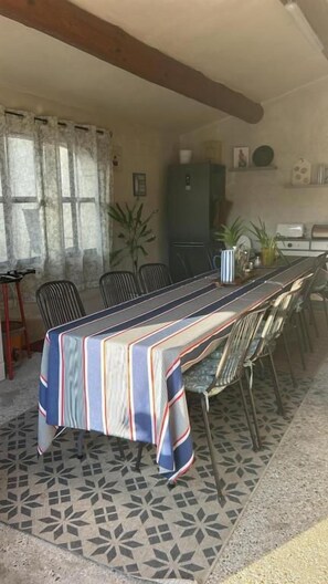 A dining area with a striped tablecloth-covered table, chairs, and a patterned floor. - Mas de la Bimarde (Monteux)