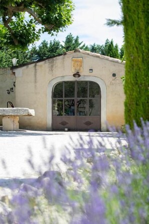 A building with a large arched entrance, a stone bench, and a garden with purple flowers.