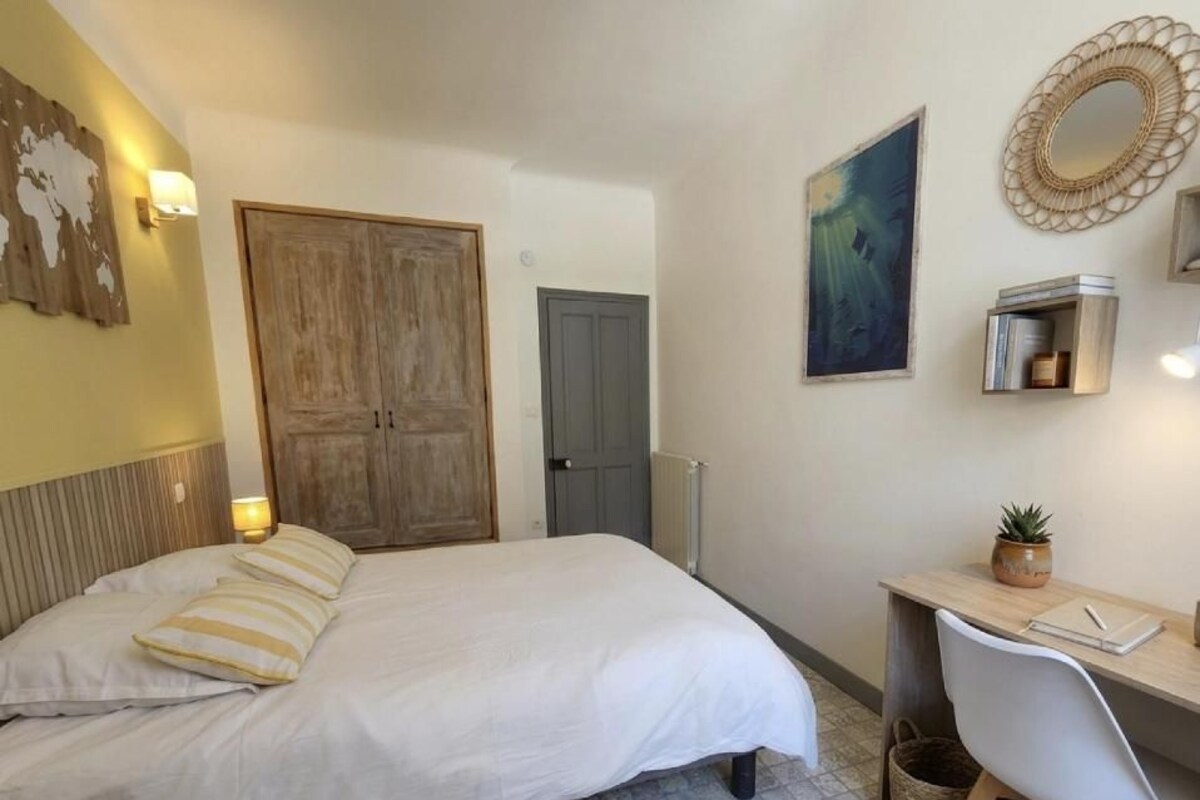A bedroom with a bed, desk, chair, and a wall-mounted shelf.