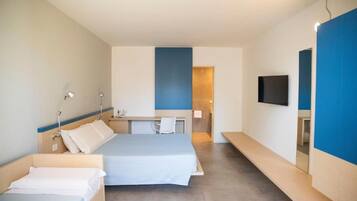Habitación de hotel con dos camas, un escritorio, una silla, un televisor y un baño visible a través de una puerta abierta.