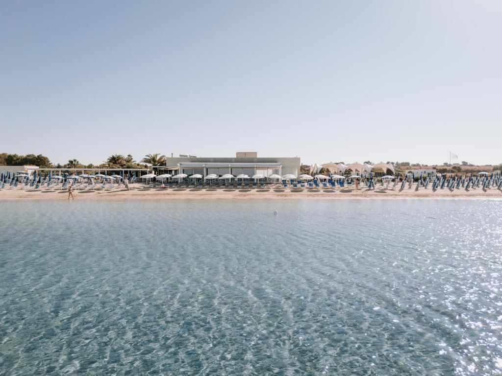 A beachfront hotel with a pool, beach umbrellas, and a clear view of the sea.