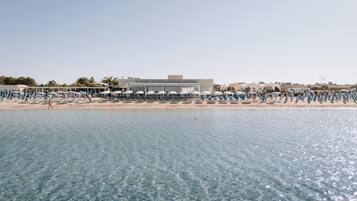 A beachfront hotel with a pool, beach umbrellas, and a clear view of the sea.