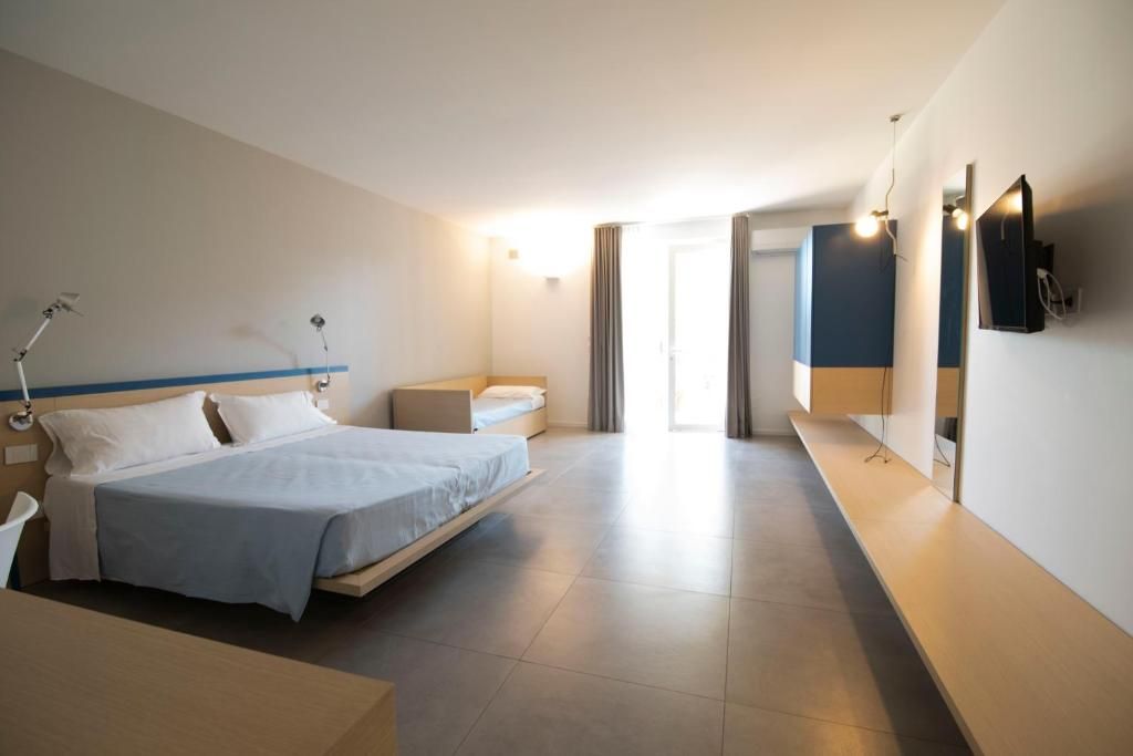A modern hotel room with a bed, bedside table, lamp, and a flat-screen TV mounted on the wall.