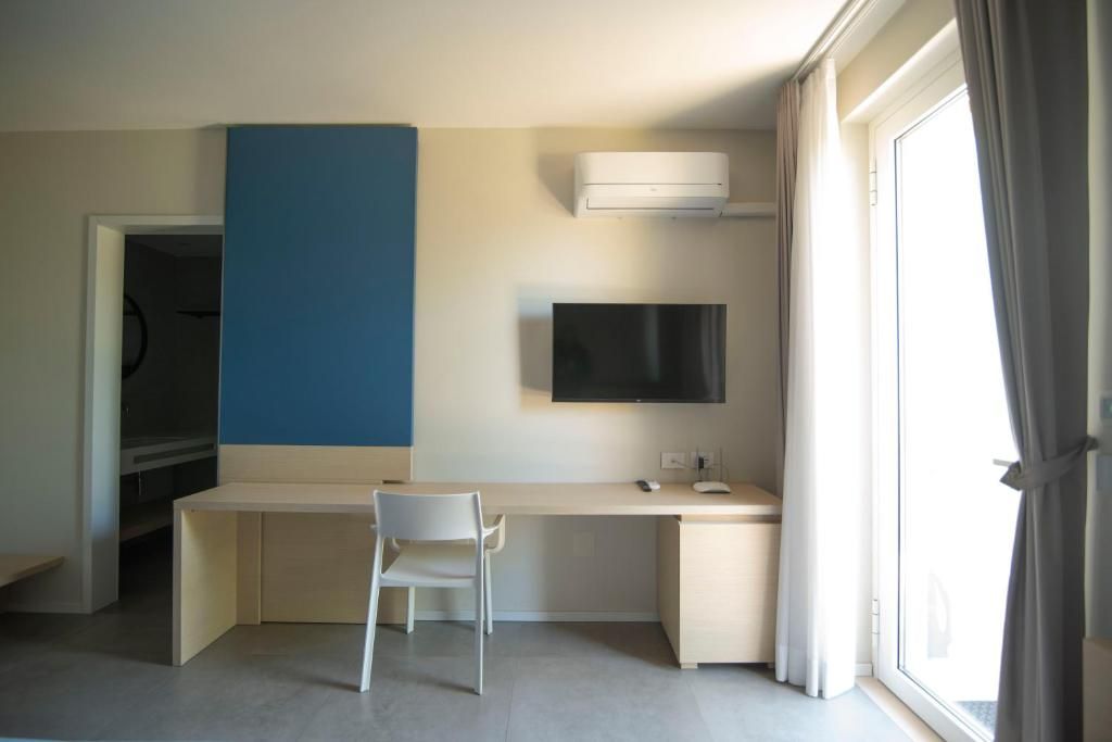 A hotel room with a desk, chair, TV, and a large window.