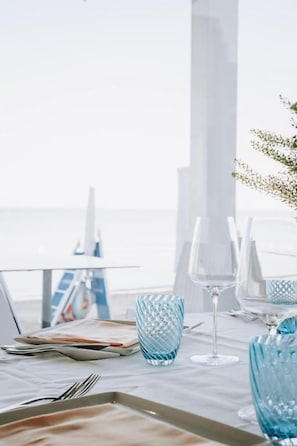 Mesa preparada para comer con vista al mar, una computadora portátil y un jarrón decorativo.