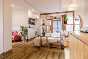 Une chambre d’hôtel moderne avec un plancher en bois, un lit avec une literie blanche, un canapé rose et une vue sur la mer par la fenêtre.