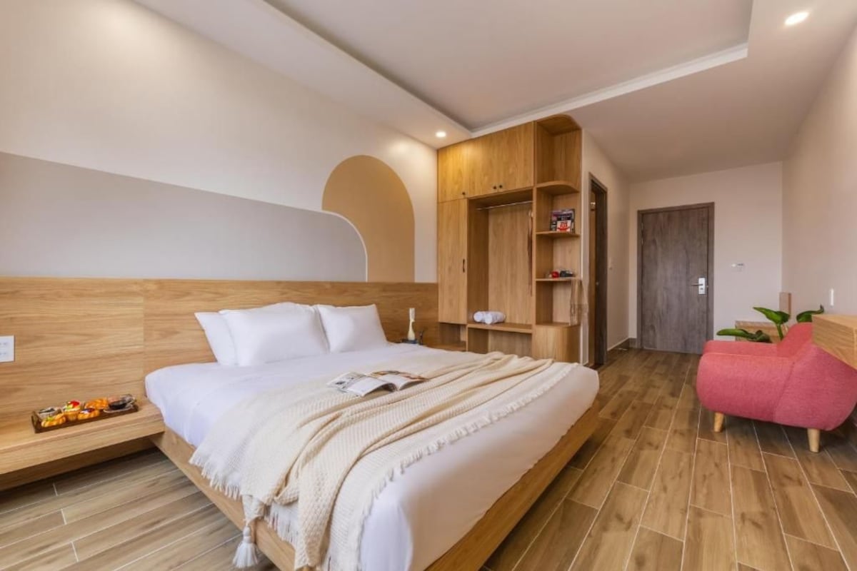 Un dormitorio moderno con cabecera de madera, cama grande, armario empotrado y una silla rosa.