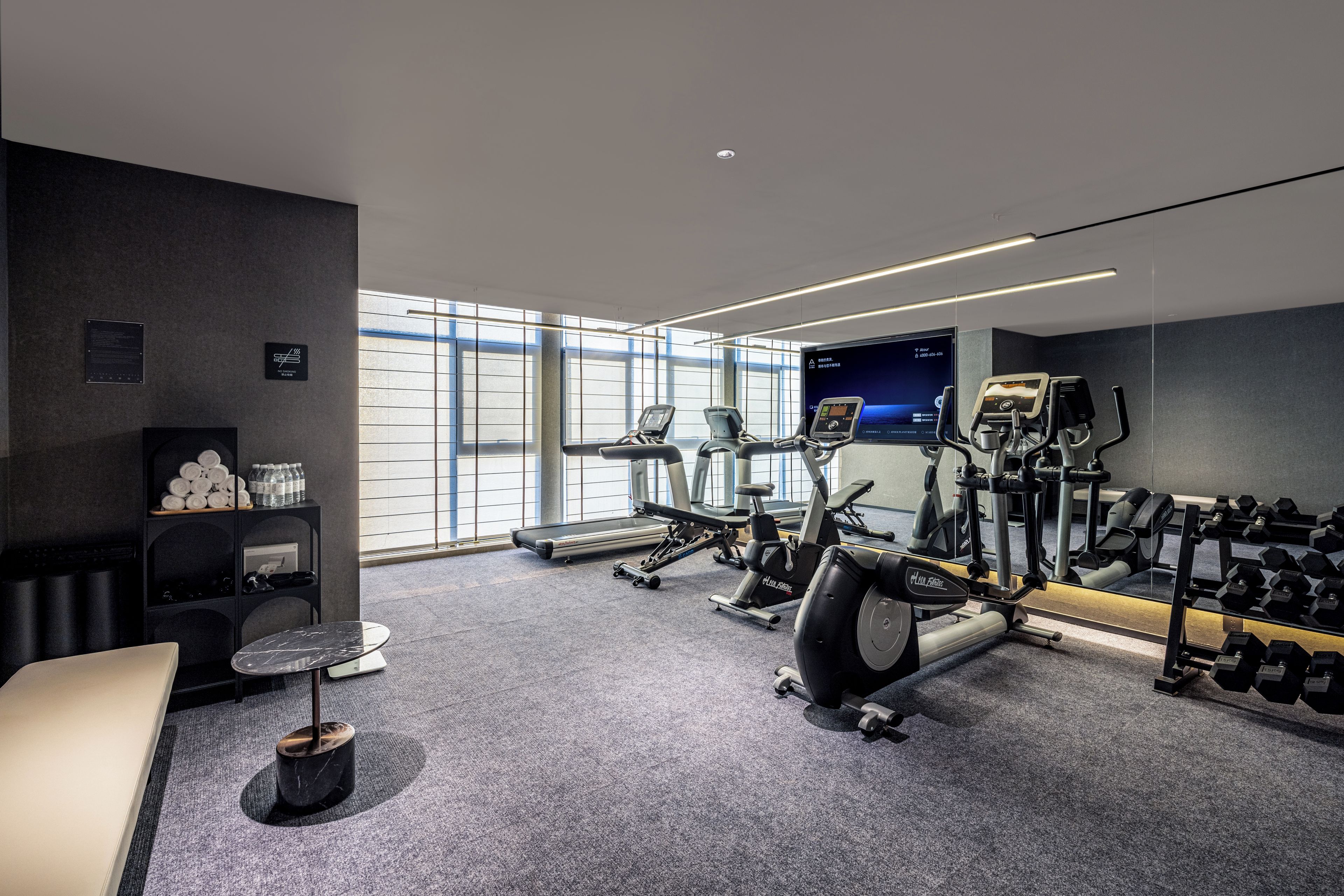 Ein modernes Fitnessstudio mit Cardiogeräten, Kurzhanteln und einem Fernsehbildschirm.
