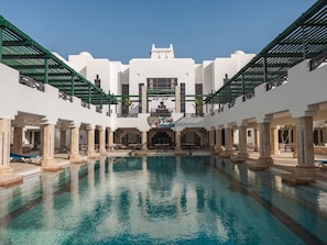 Une piscine dotée d’un escalier central, entourée de bâtiments blancs ornés de colonnes et de balcons.