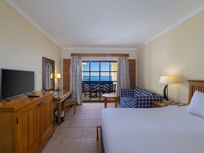 Une chambre d ’hôtel comprenant un lit, une télévision, un bureau avec une chaise, un canapé et un balcon avec vue sur l’océan.
