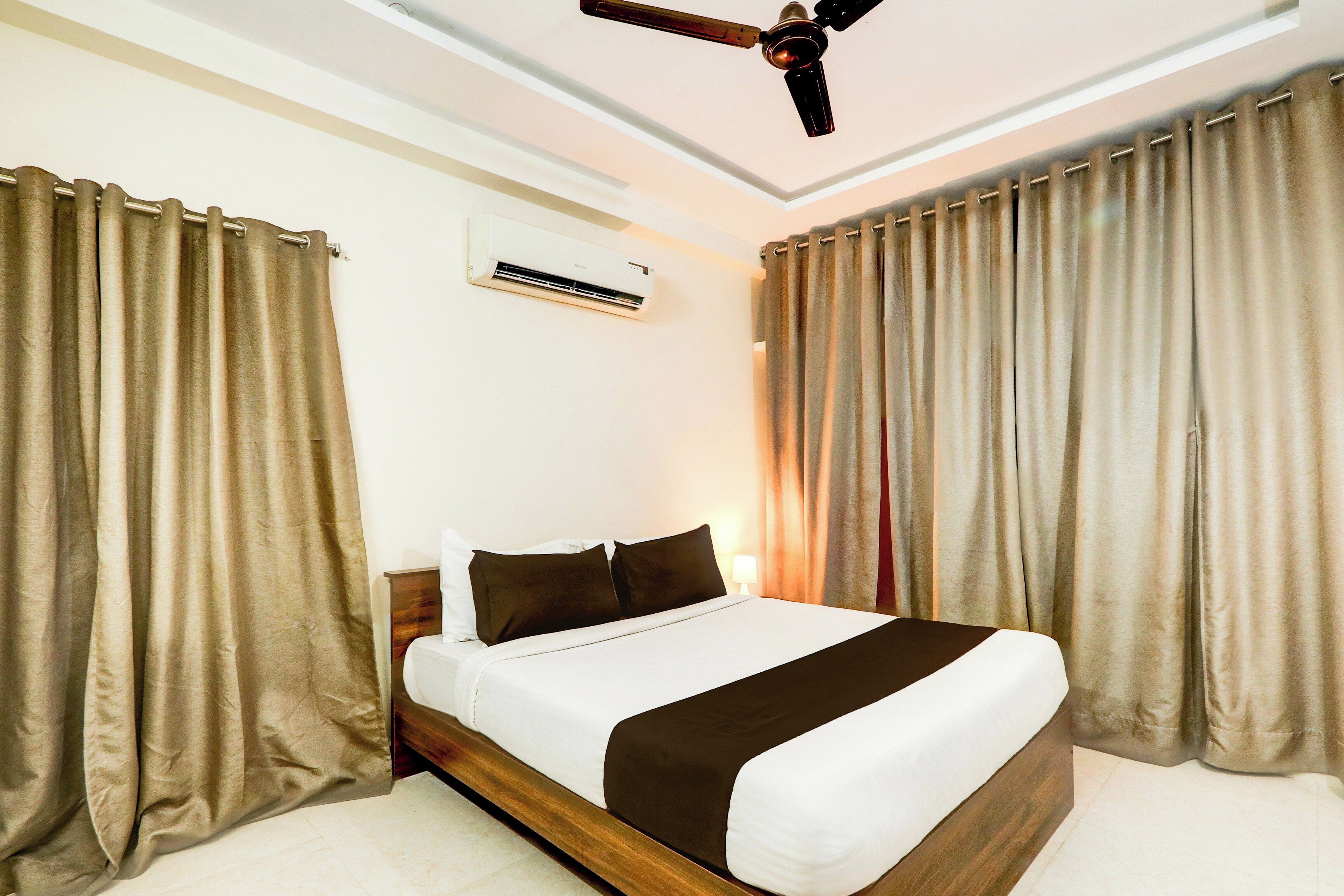 A hotel room with a bed, curtains, an air conditioning unit, and a ceiling fan.