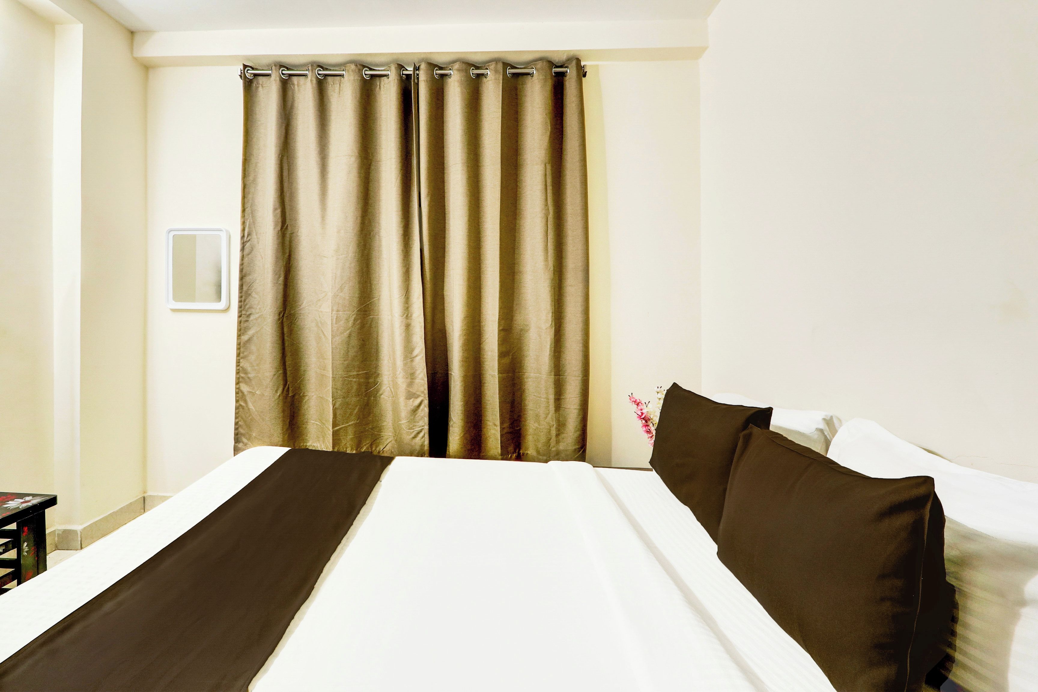 A hotel room with a bed, a curtain, and a wall-mounted light switch.