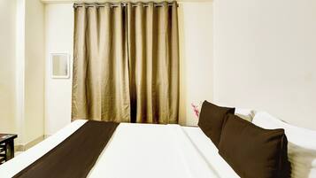 A hotel room with a bed, a curtain, and a wall-mounted light switch.