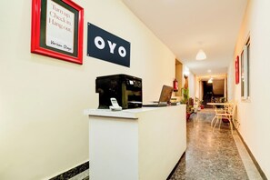 Un área de recepción de hotel con un cartel que dice 'OYO' y un cartel enmarcado encima con el texto 'Llega. Regístrate. Relájate'.