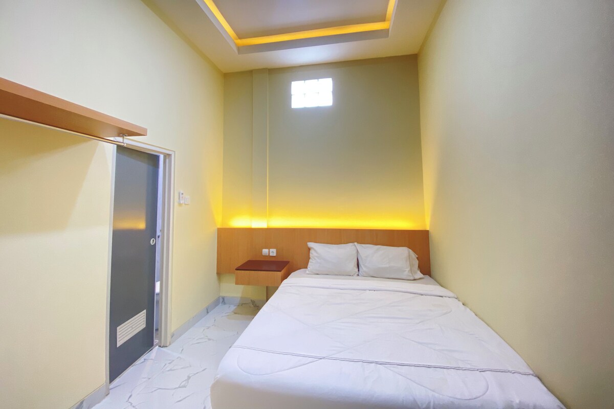 Een hotelkamer met een bed, nachtkastje, een daklamp en een raam.