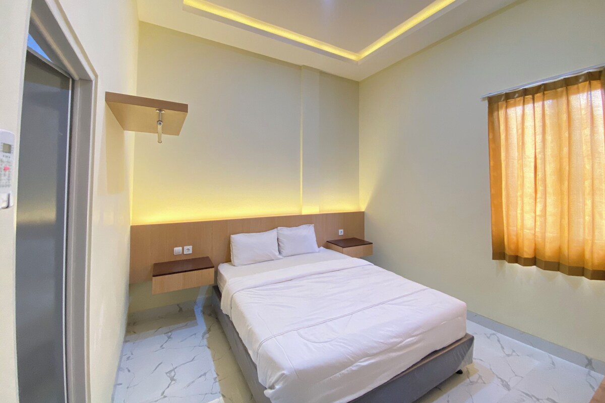 Een hotelkamer met een bed, nachtkastjes, een wandlamp en een raam met gordijnen.