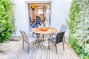 A wooden deck with a round table and chairs, surrounded by greenery. - Cozy House, Town Center, 7 min Beach by Groom* (Ploemeur)