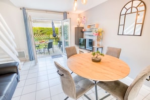 A dining area with a round table, chairs, a television, and a view of the outdoors. - Cozy House, Town Center, 7 min Beach by Groom* (Ploemeur)