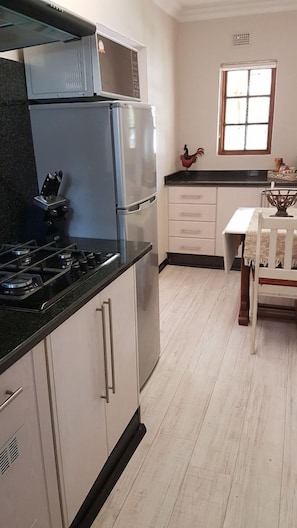 A kitchen with a gas stove, microwave, refrigerator, and a dining table with chairs. - Haggards on Hilldrop (Newcastle)