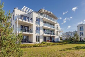 Ein mehrgeschossiges Wohngebäude mit Balkonen, einer flachen Dachterrasse und einem gepflegten Rasen.