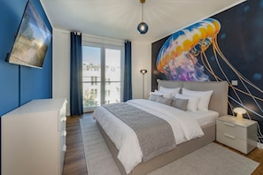 Un dormitorio con una cama grande, un escritorio, una mesita de noche, una lámpara y un mural en la pared.