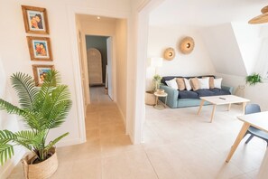 A modern living room with a sofa, a coffee table, and a dining table. There is a plant in a woven basket and a wall-mounted lamp. - Beautifully renovated 2-bedroom apartment, near the beaches by Groom* (Ploemeur)