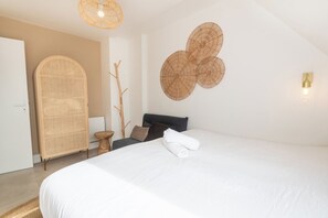 A hotel room with a large bed, a rattan wardrobe, a wall-mounted circular decoration, and a small wooden stool. - Beautifully renovated 2-bedroom apartment, near the beaches by Groom* (Ploemeur)