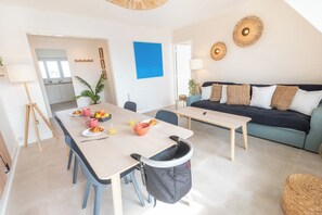 A modern living room with a sofa, a dining table, and a kitchen in the background. - Beautifully renovated 2-bedroom apartment, near the beaches by Groom* (Ploemeur)