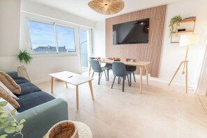 Ein modernes Wohnzimmer mit einer Couch, einem Esstisch, Stühlen, einem an der Wand montierten Fernseher und einer Stehlampe.