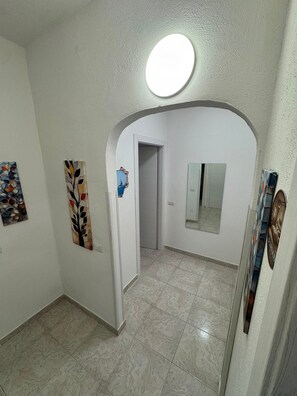 A hallway with a white door, a mirror, and artwork on the walls.