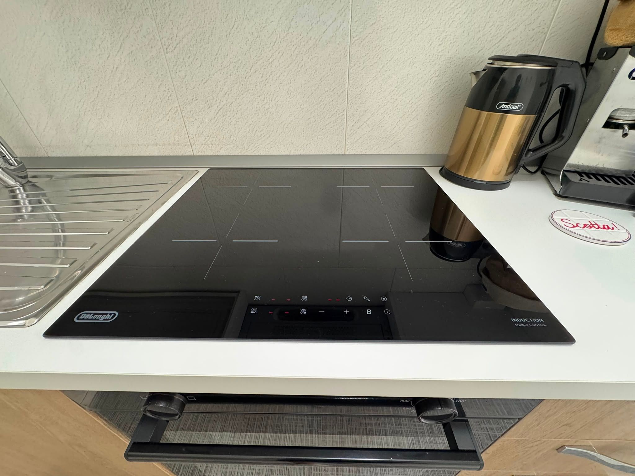 Une cuisine équipée d’une plaque de cuisson à induction noire, d’une machine à café DeLonghi et du logo de la marque de café Scelta.