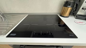 Une cuisine équipée d’une plaque de cuisson à induction noire, d’une machine à café DeLonghi et du logo de la marque de café Scelta.