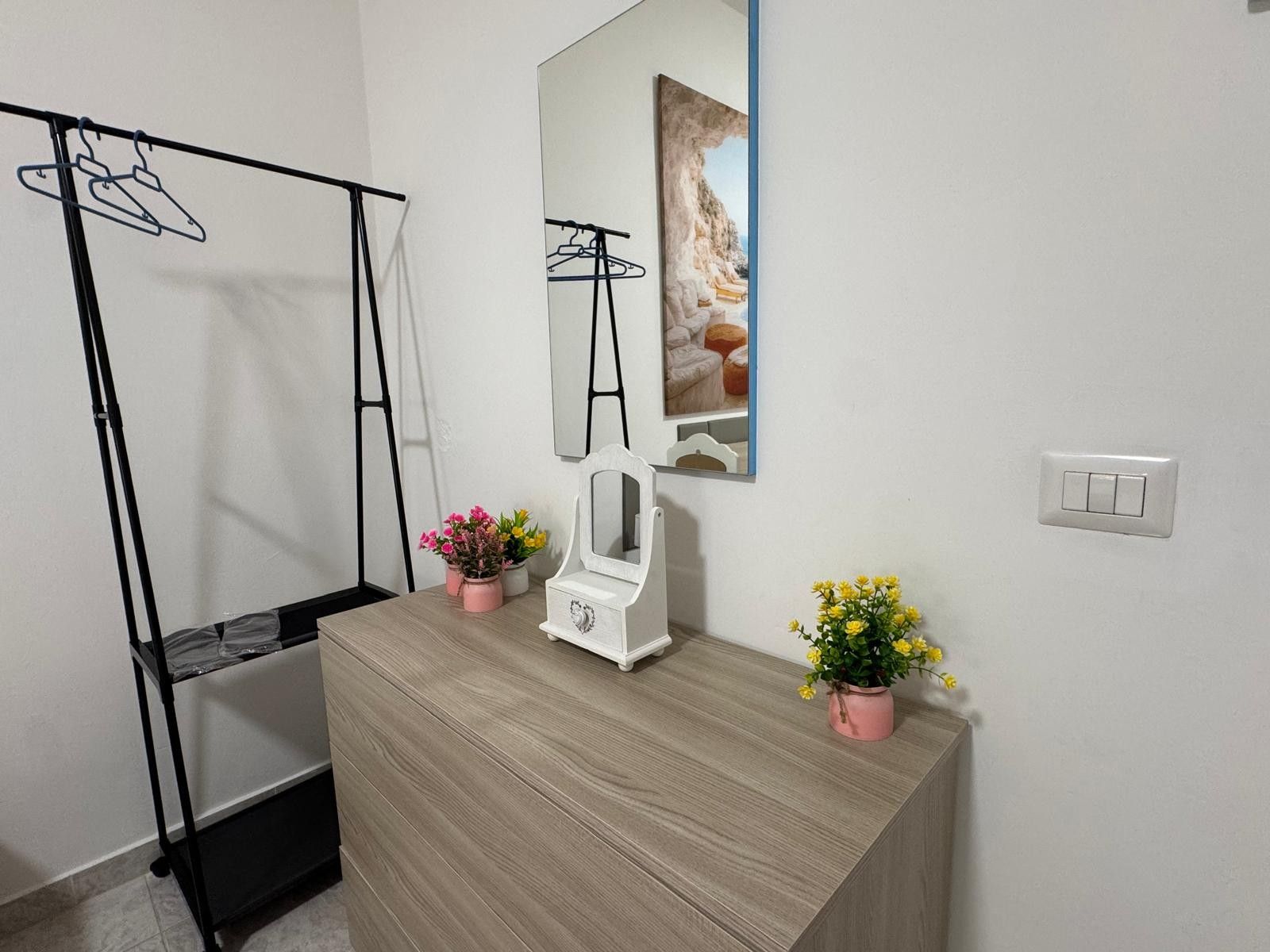 A room with a wooden dresser, a mirror, two potted plants, a coat rack, and a wall-mounted picture.