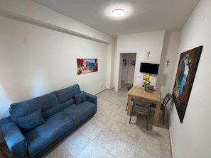 A living room with a blue sofa, a dining table with chairs, and a TV mounted on the wall.
