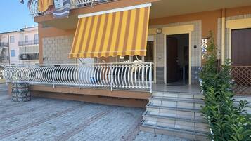 Un immeuble résidentiel doté d’un balcon, d’un auvent à rayures et d’un espace d’entrée pavé.
