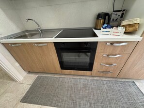Cocina compacta con pileta, estufa, horno y cafetera.