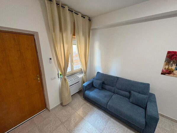 A room with a wooden door, a blue sofa, a radiator, and a window with curtains.