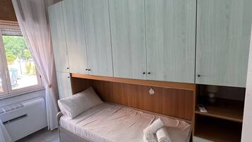 A single bed with a wooden headboard, a bedside table, and a built-in wardrobe with multiple compartments.